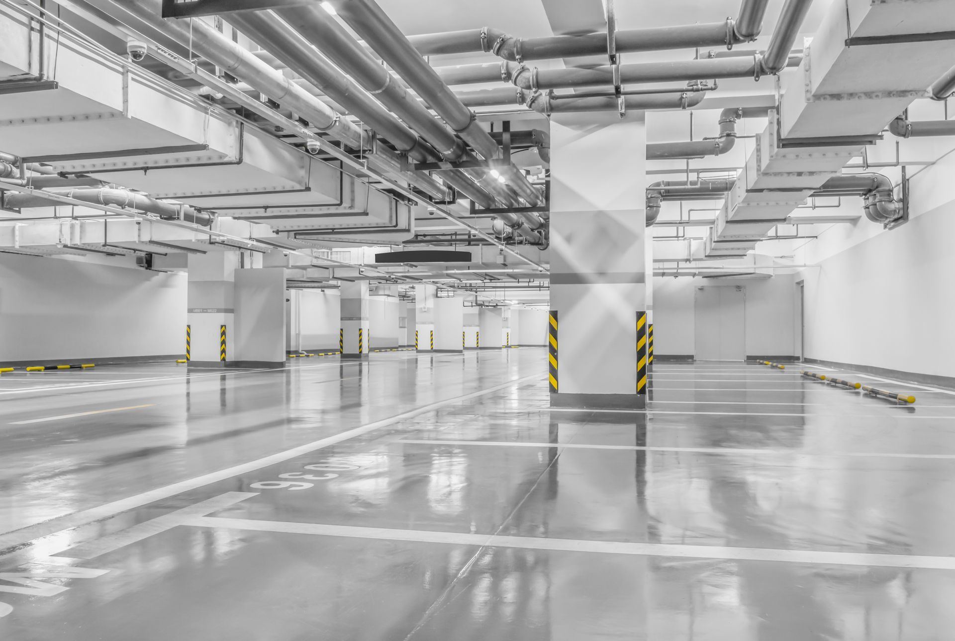 A bright, modern underground parking garage with white walls, polished grey floors, and overhead HVAC ductwork.
