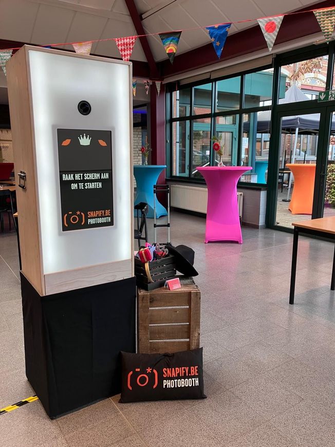 In een ruimte met slingers en kleurrijke cocktailtafels staat een houten fotocabine met leuke props