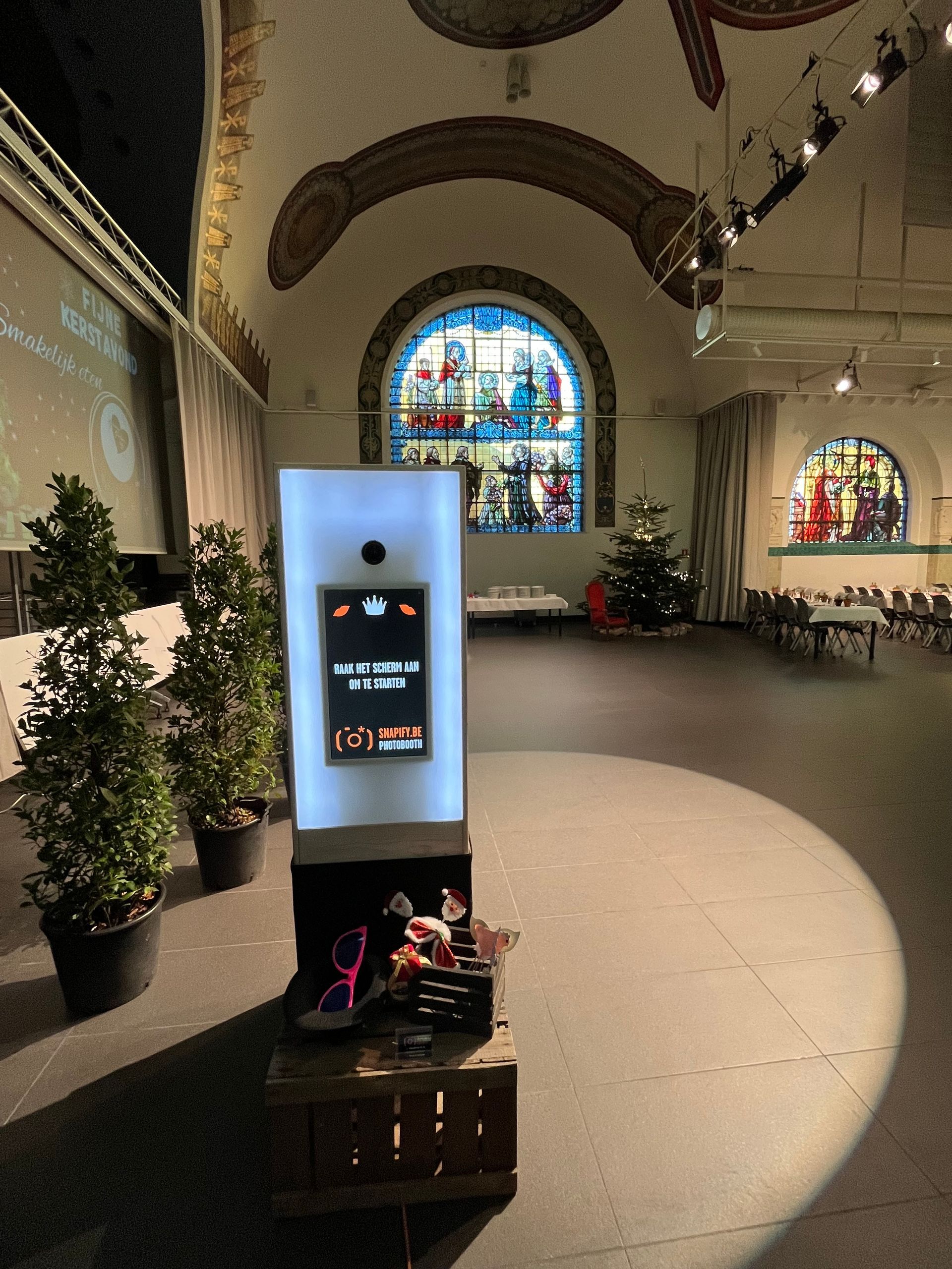In een grote hal met gewelfde plafonds en glas-in-loodramen staat een fotocabine, die verlicht wordt door een spot.