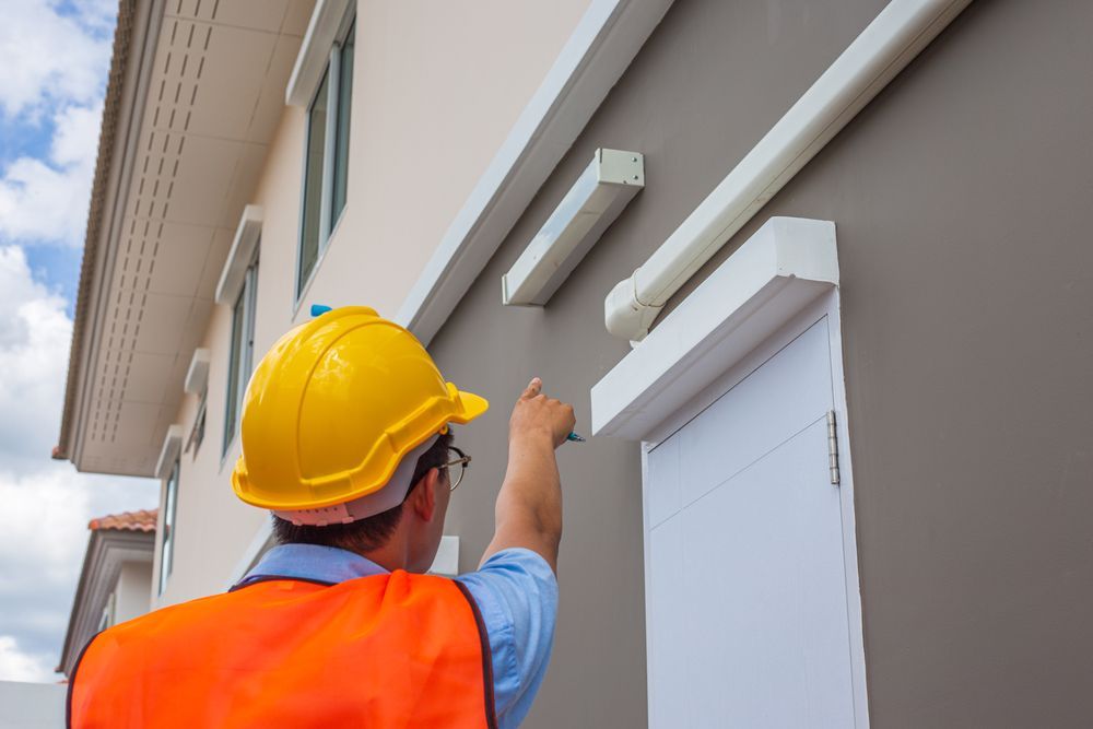 Person in hard hat and safety vest inspecting a building's exterior, pointing.