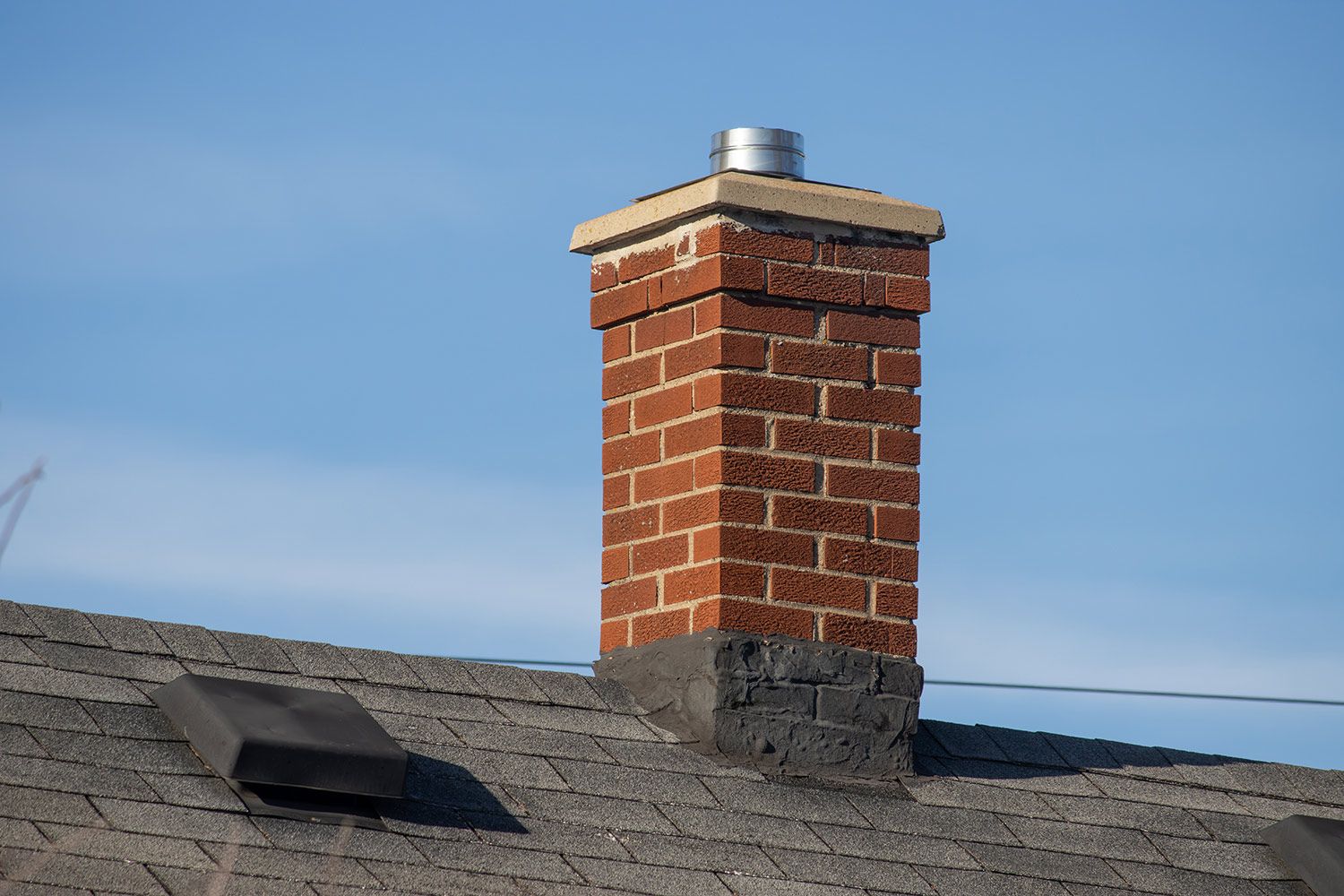 Chimney on a shingled roof against a blue sky