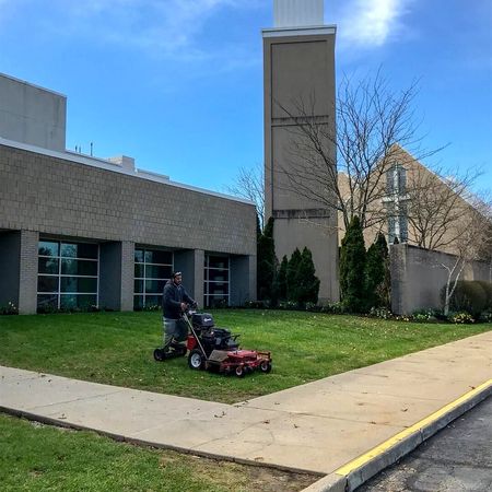 Man mowing lawn at a church with gray building, blue sky.