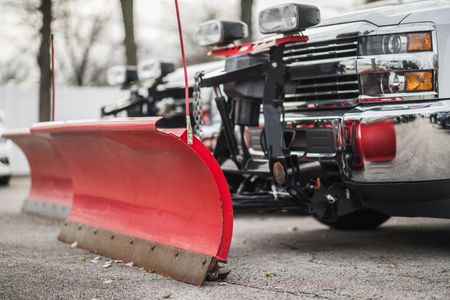 Red snowplow attached to a truck, ready to clear snow from a parking area.