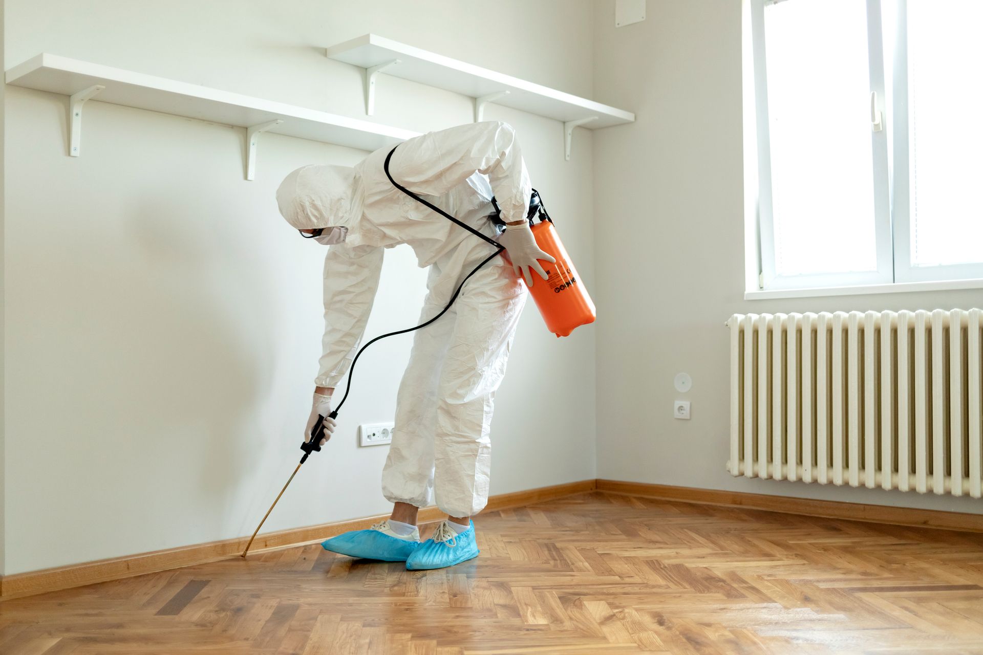 Man in chemical protection suit performing professional termite treatment in an empty space.