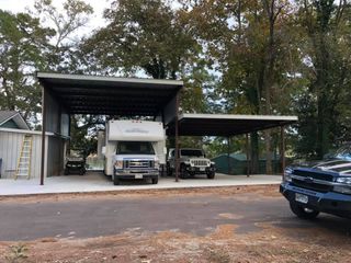 A truck and a rv are parked under a carport.