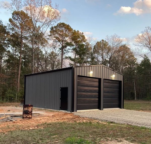 A metal building with two garage doors is surrounded by trees