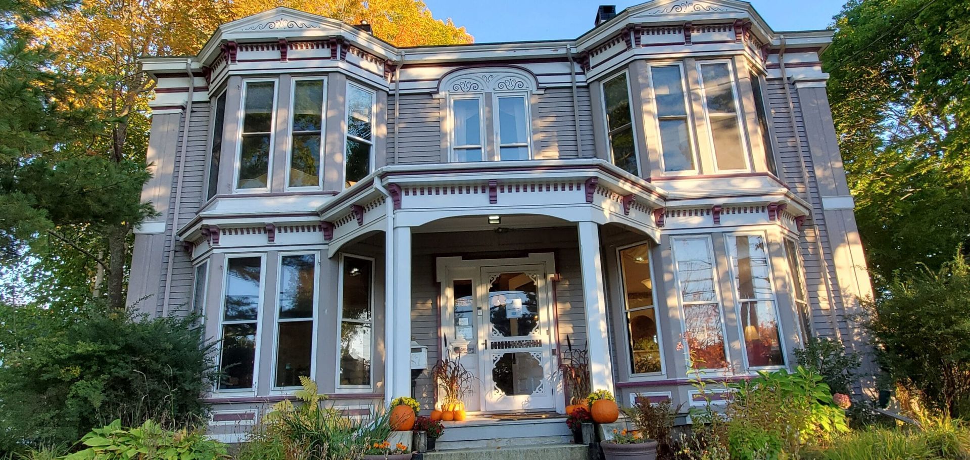 A large house with a porch and pumpkins in front of it.