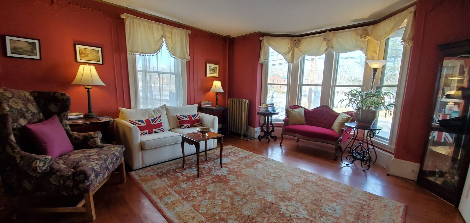 A living room with red walls , a couch , chairs , lamps and a rug.