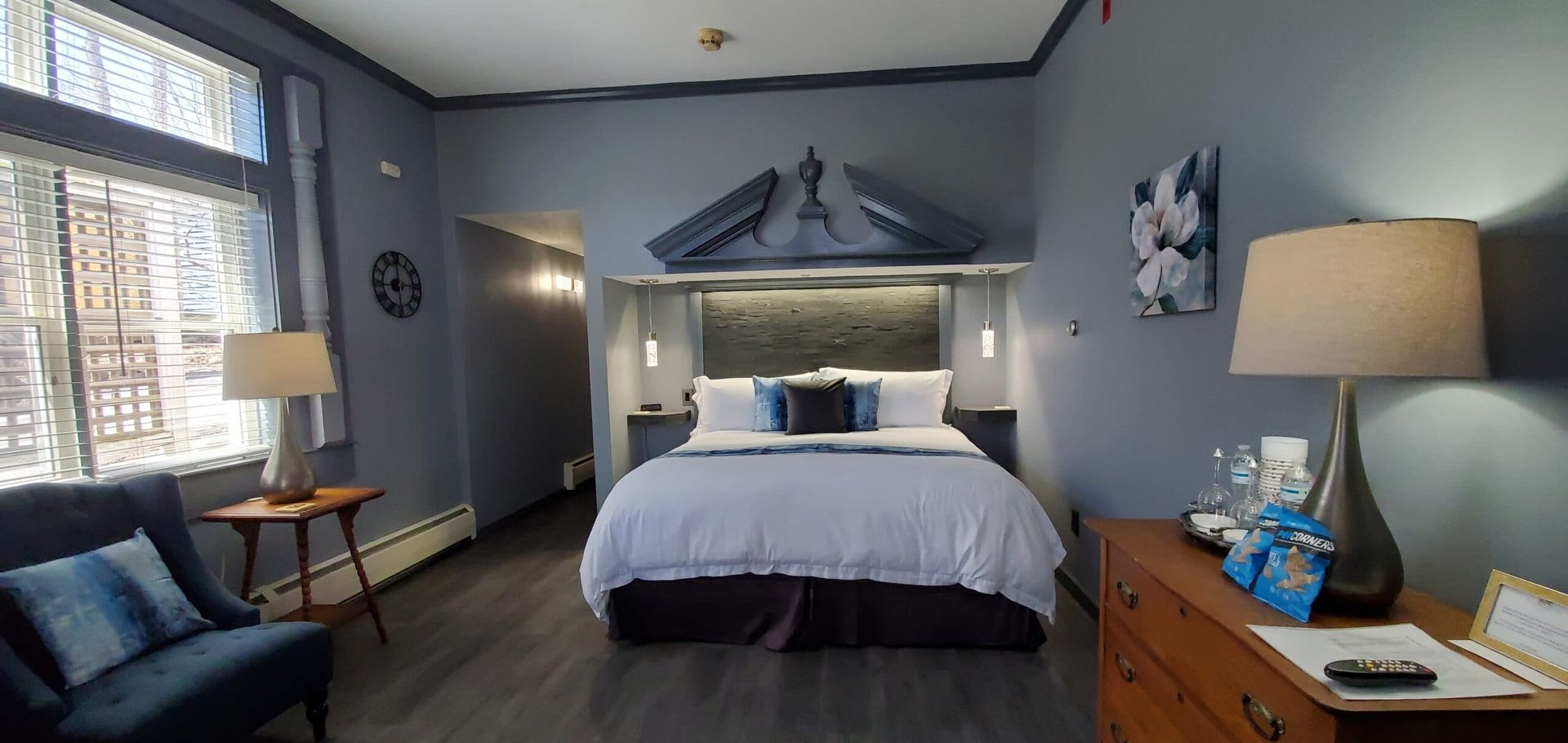 A hotel room with a king size bed , dresser , chair and lamps.