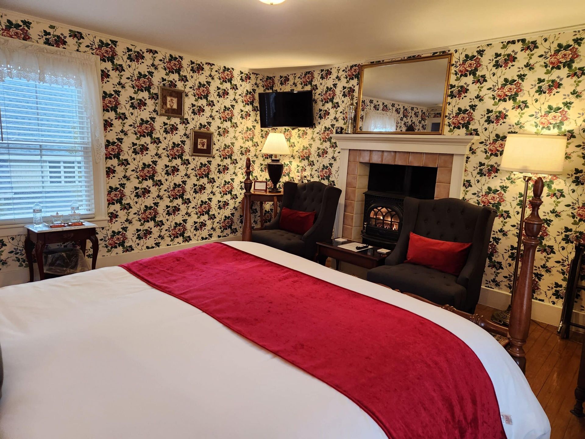 A bedroom with a bed , chairs , lamps and a fireplace.