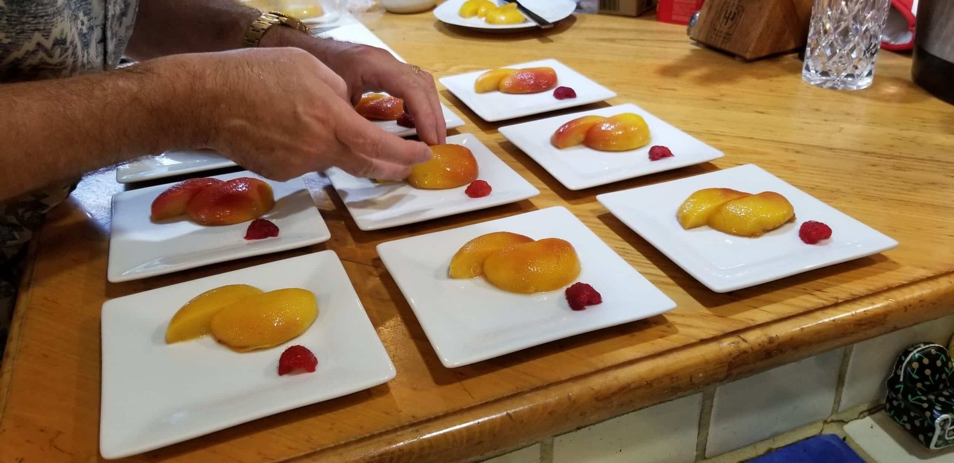 A person is arranging plates of fruit on a wooden table.