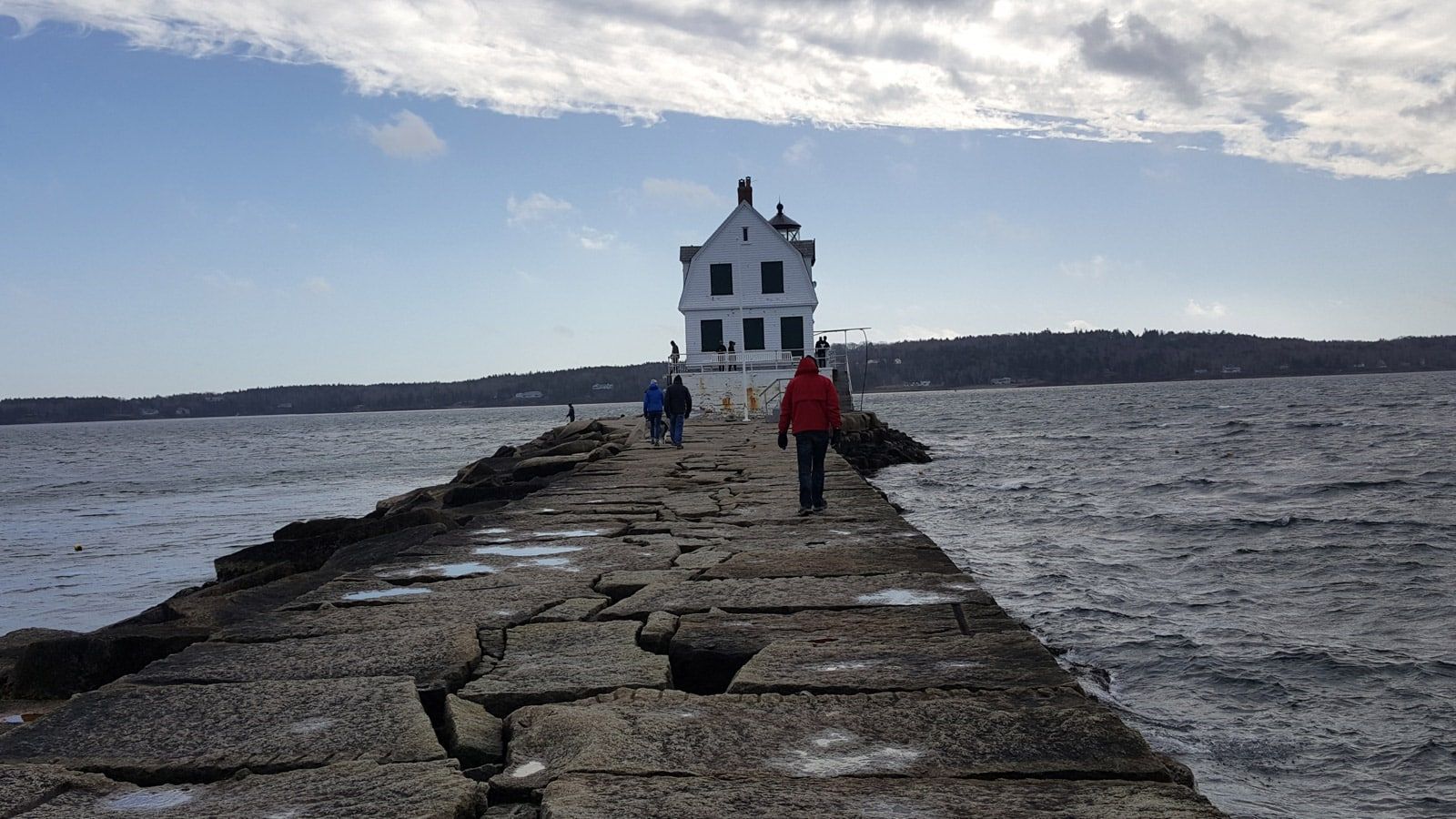 A group of people are walking down a pier towards a lighthouse.