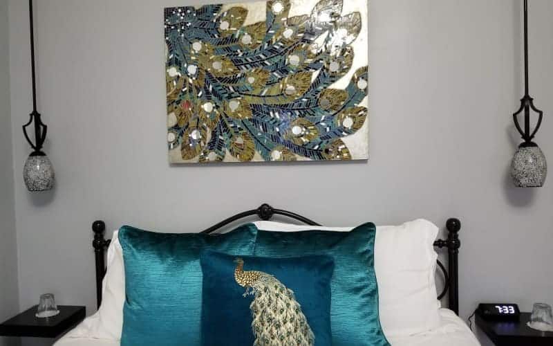 A bed with a peacock pillow and a painting on the wall above it.