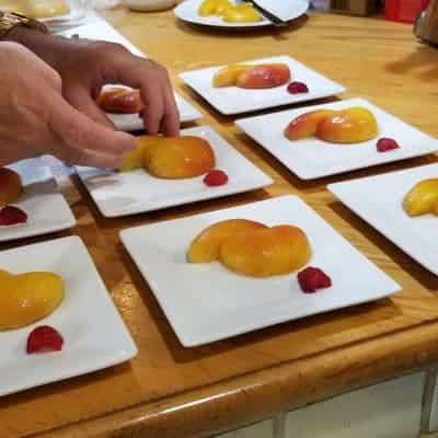 A person is arranging plates of fruit on a wooden table.