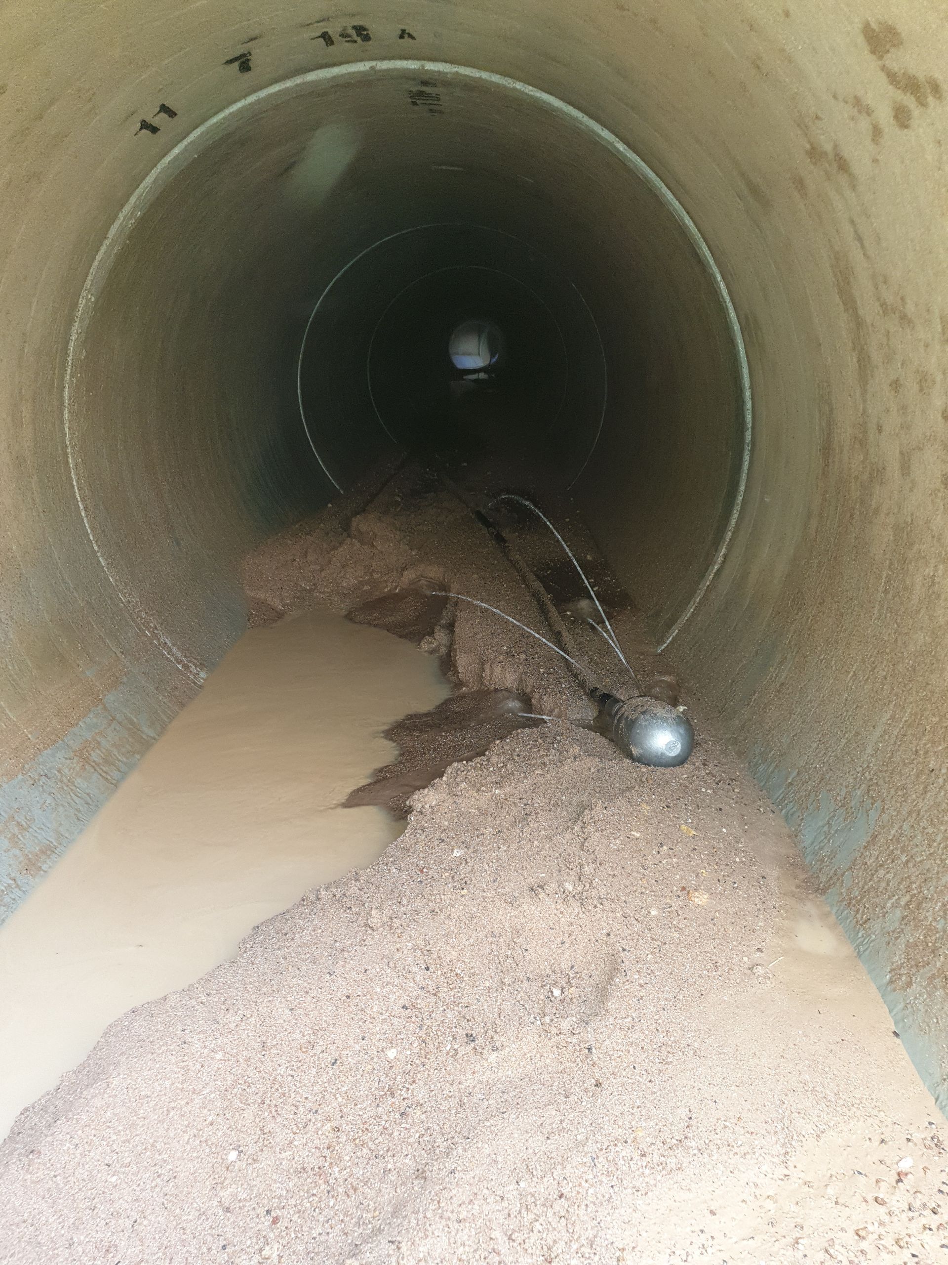 Inside a large, cylindrical pipe, debris and muddy water accumulate; light at the far end — Pro Pipe Solutions in Queanbeyan, NSW