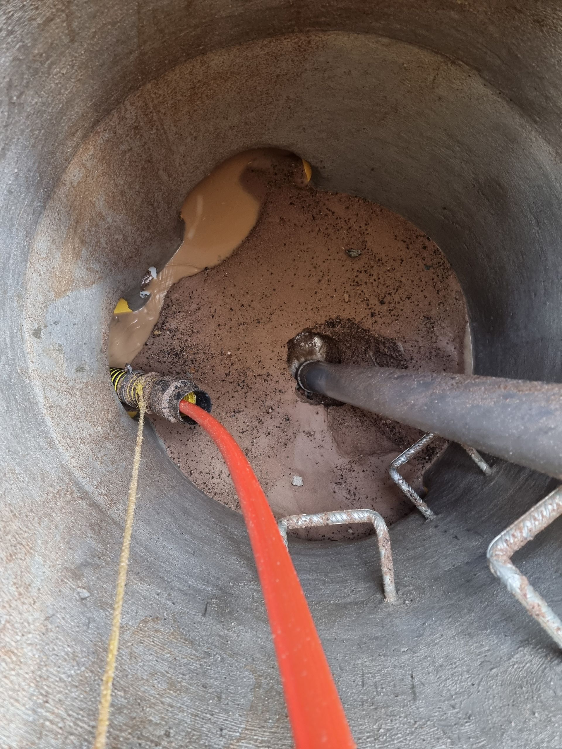 Inside a concrete cylinder, brown sludge covers a base with a red hose and metal bar protruding — Pro Pipe Solutions in Queanbeyan, NSW