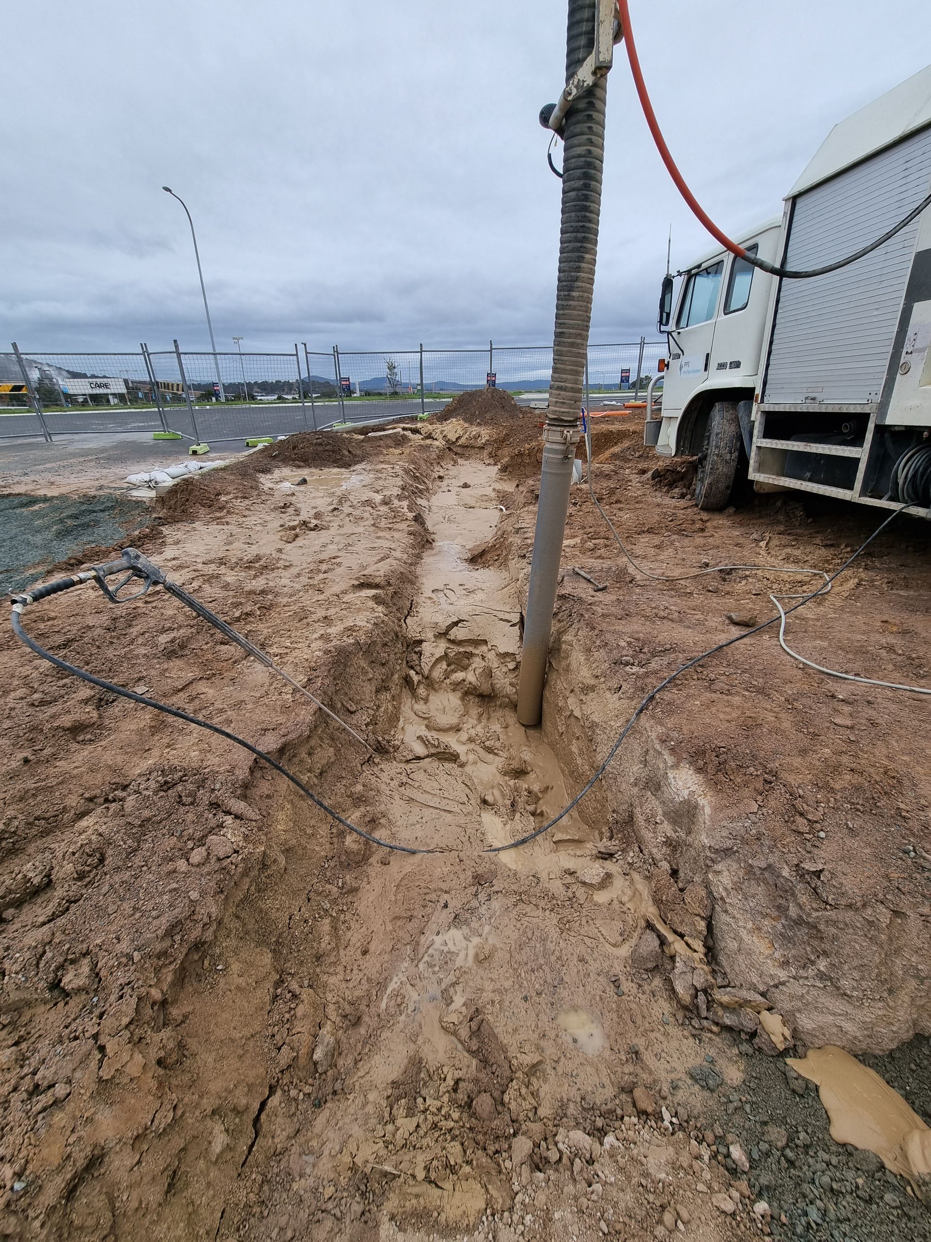 Trench in muddy soil, with a drilling rig and truck. Cloudy outdoor setting — Pro Pipe Solutions in Queanbeyan, NSW