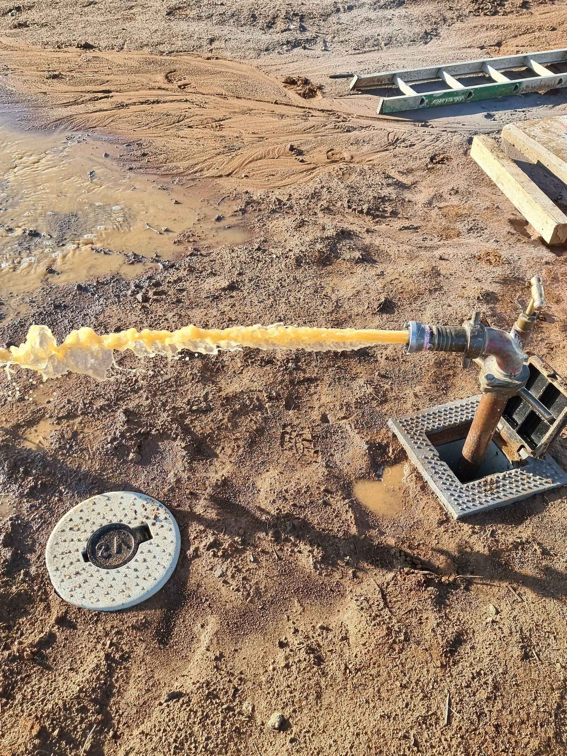 Yellow foamy water shoots from a pipe on a dirt ground, near a manhole cover and a ladder — Pro Pipe Solutions in Queanbeyan, NSW