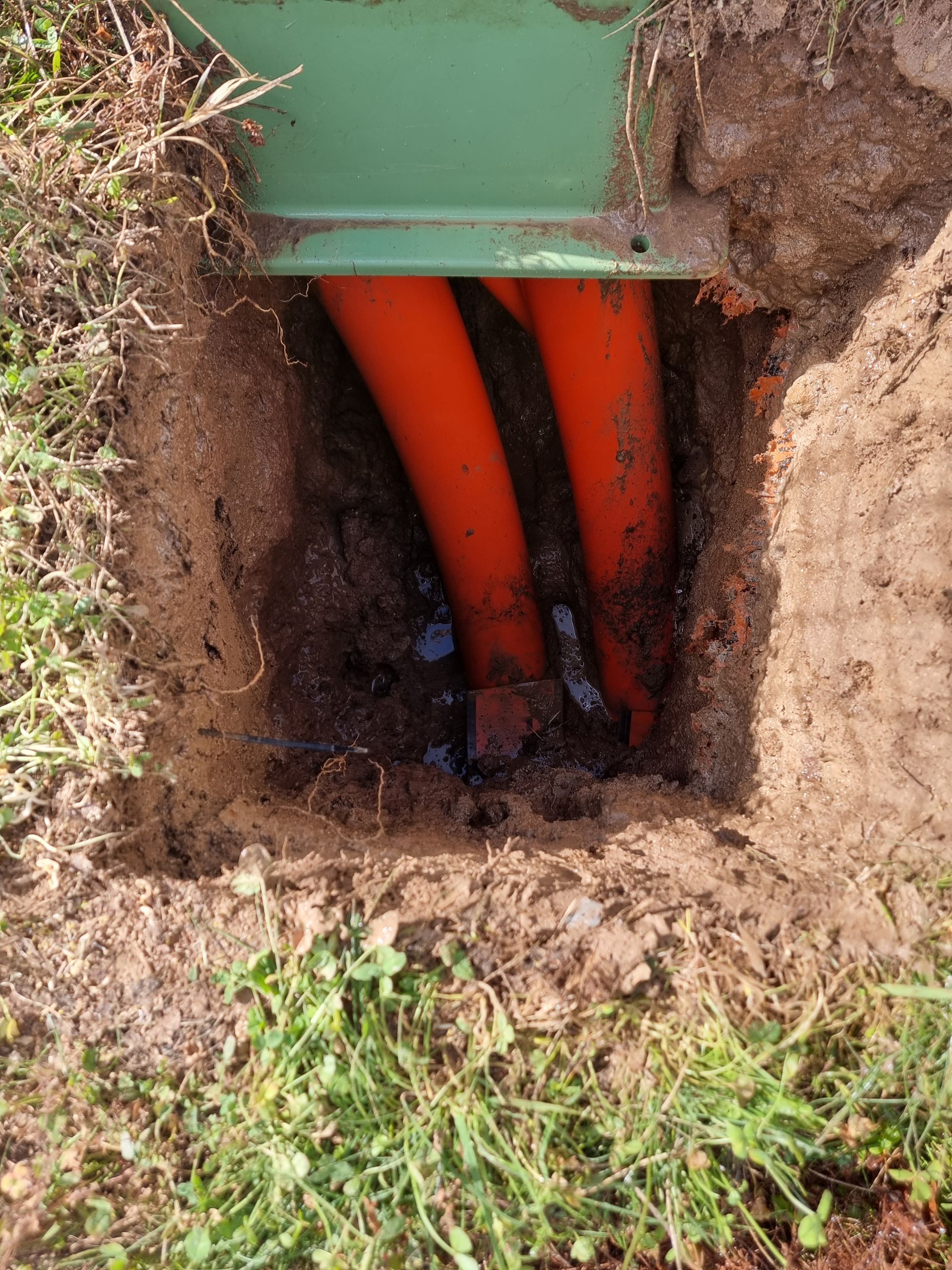 Orange conduit pipes in a rectangular hole in the ground with a green electrical box above — Pro Pipe Solutions in Queanbeyan, NSW