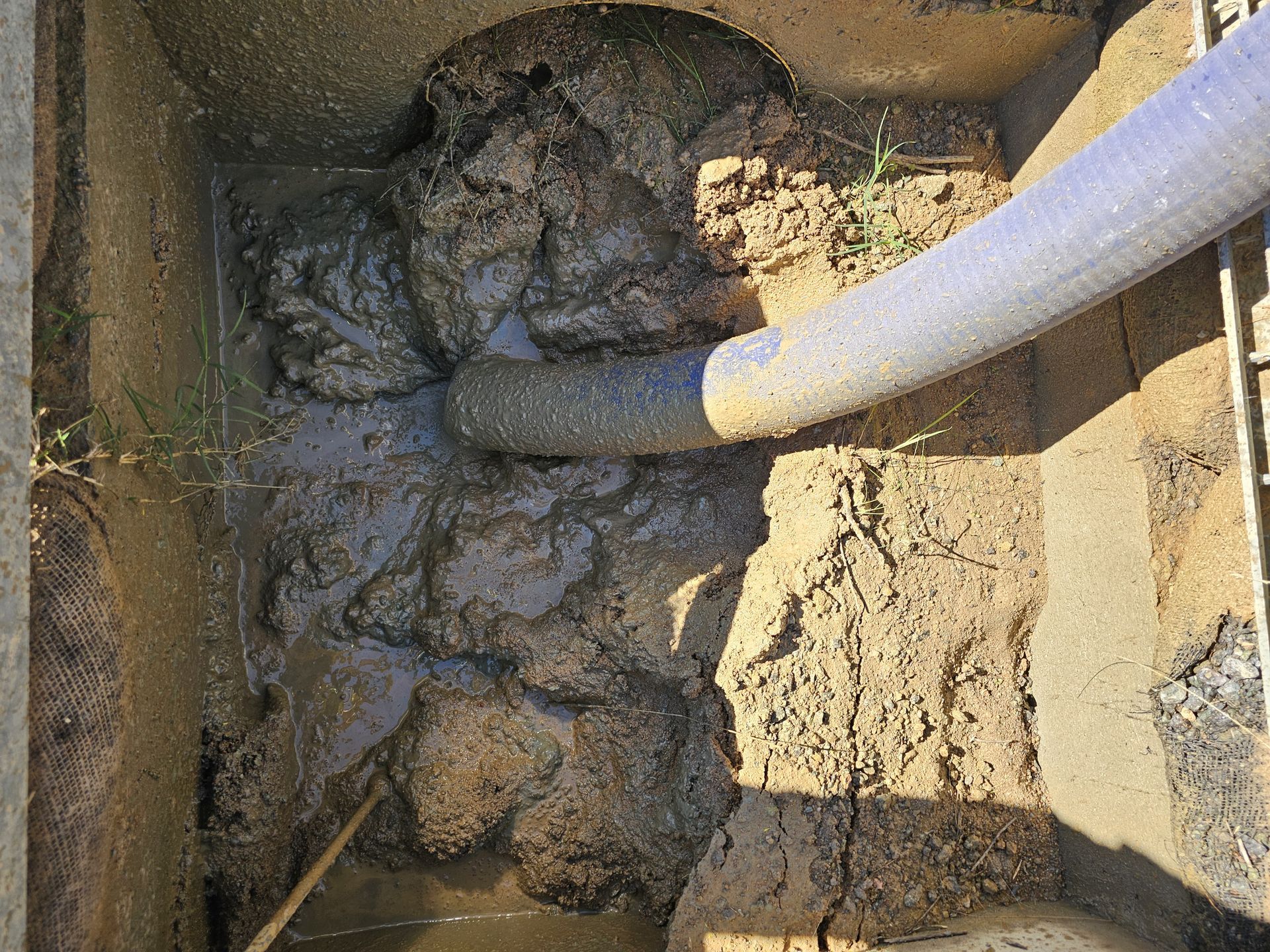 Muddy debris being sucked out of a square concrete container by a large hose — Pro Pipe Solutions in Queanbeyan, NSW