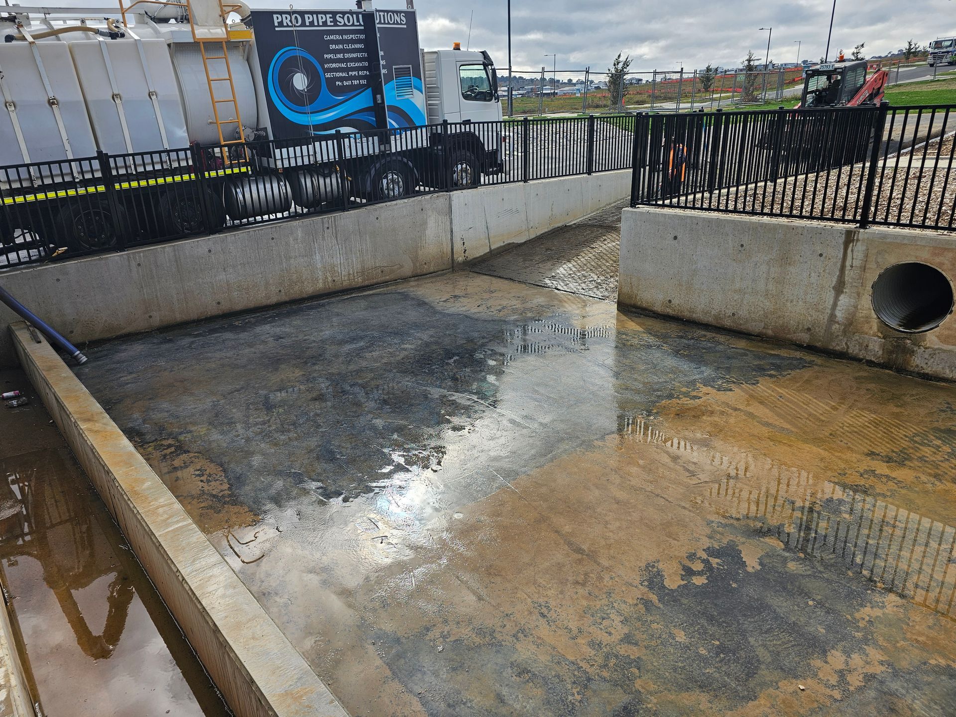 Water-filled concrete basin, possibly for stormwater management, with a fence and a truck in the background — Pro Pipe Solutions in Queanbeyan, NSW