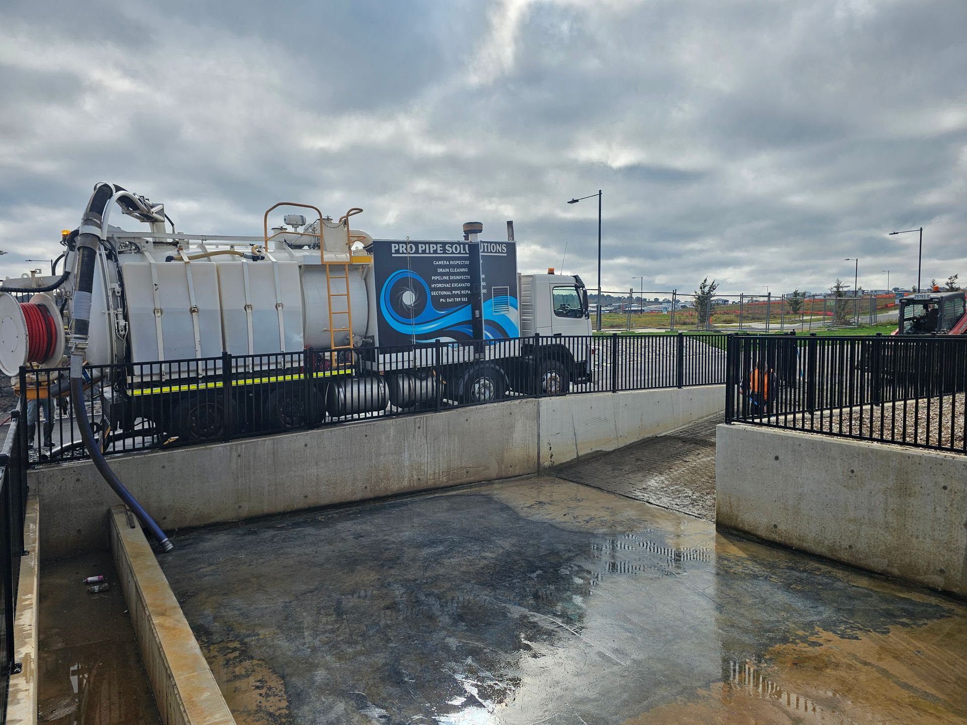 A truck with equipment is working on a concrete structure with water on the ground under a cloudy sky — Pro Pipe Solutions in Queanbeyan, NSW