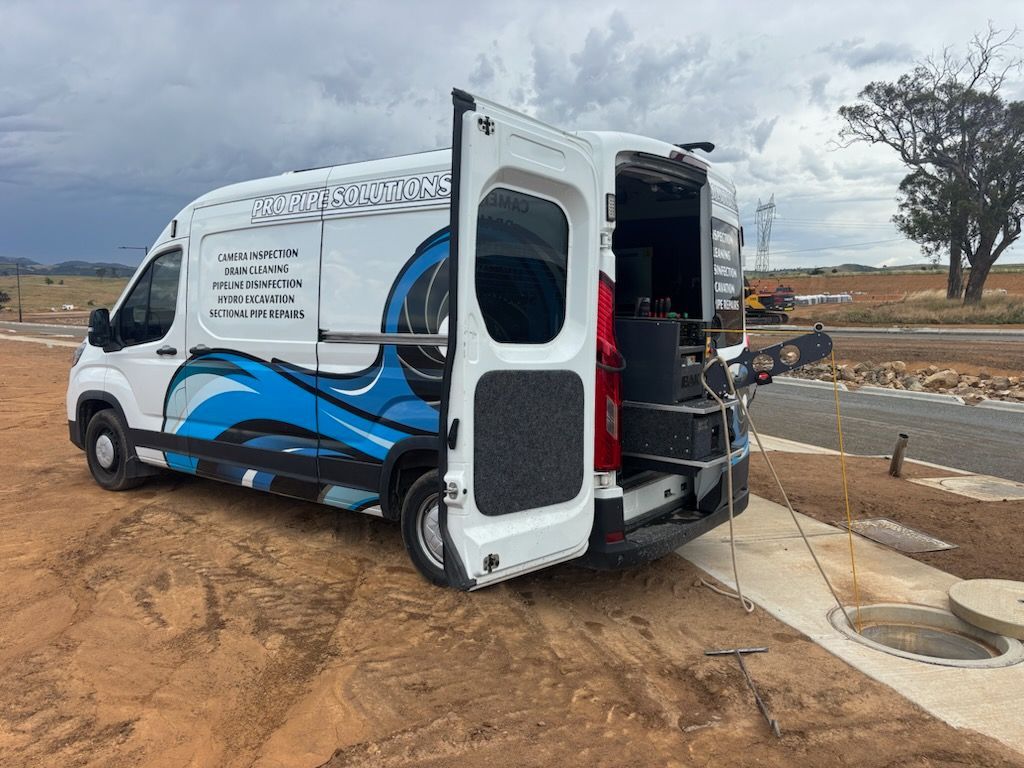 White service van with open back doors parked on dirt, blue water graphic — Pro Pipe Solutions in Queanbeyan, NSW