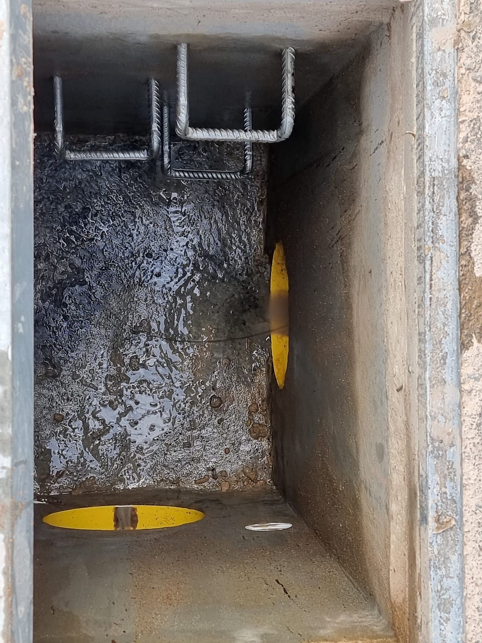 Concrete drainage pit with water, metal bars, and yellow markings — Pro Pipe Solutions in Queanbeyan, NSW