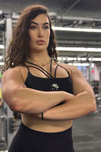 A woman with a lot of muscles is standing in a gym with her arms crossed. Anais Velvet Fitnes