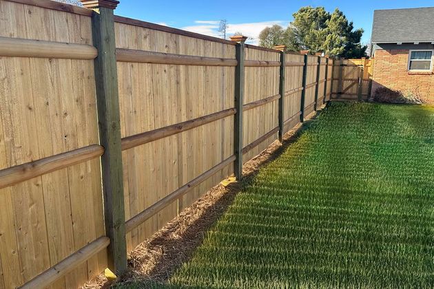 A wooden fence surrounds a lush green lawn in a backyard.