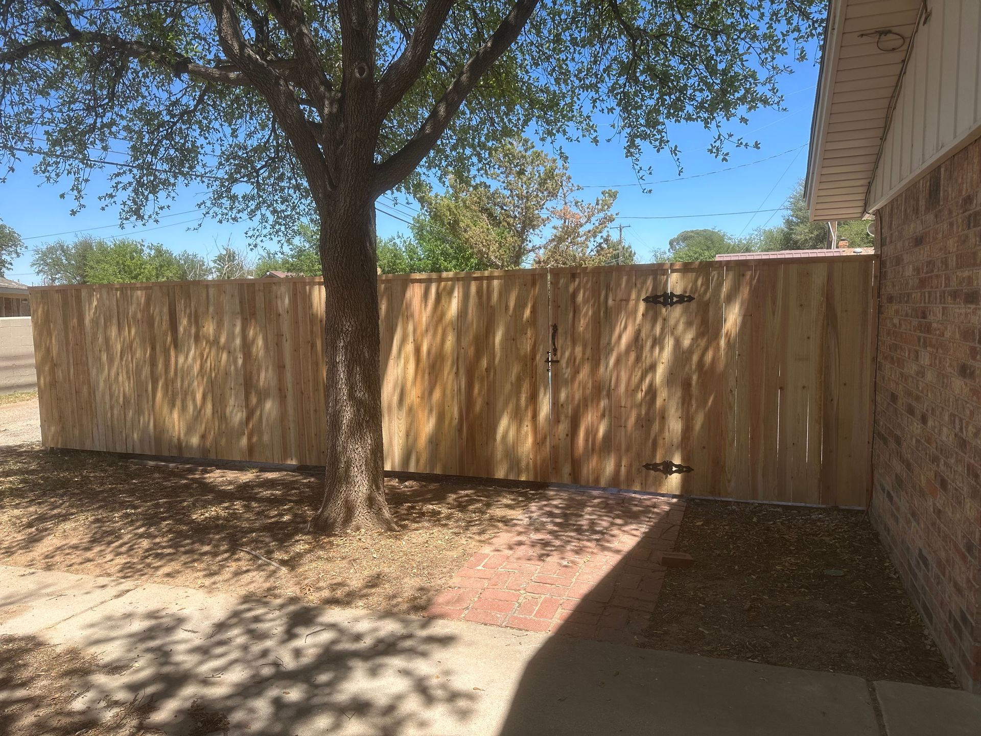 A wooden fence surrounds a brick house with a tree in the background.