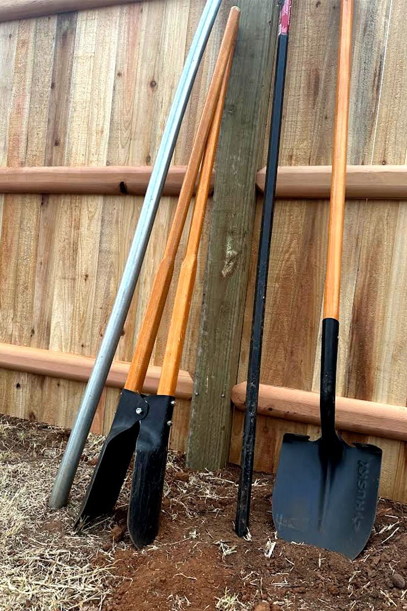 Three gardening tools are sitting on the ground in front of a wooden fence.