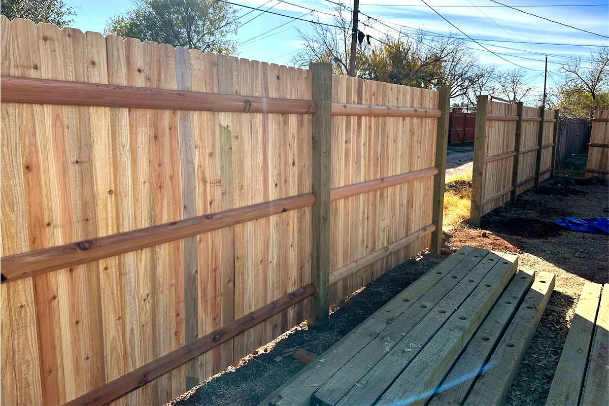 A wooden fence is surrounding a wooden deck in a backyard.