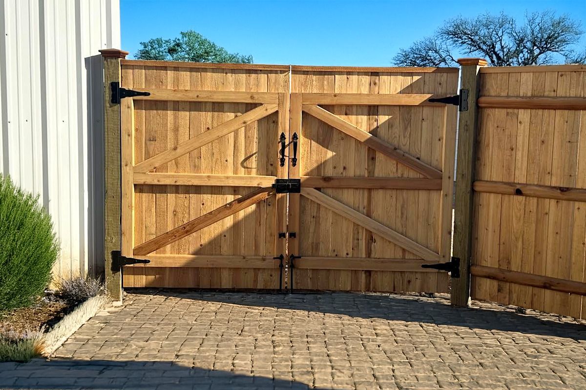 A wooden gate is sitting on a brick driveway next to a building.