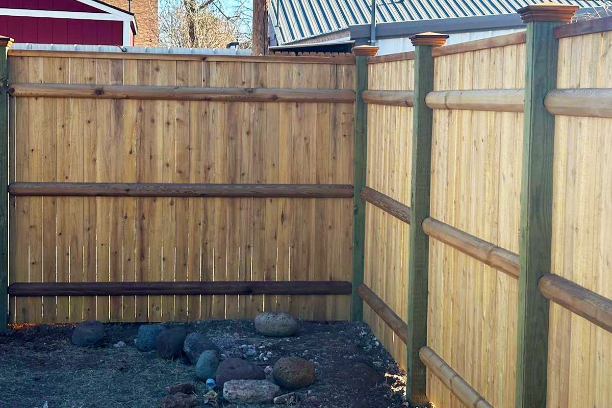 A wooden fence is surrounding a rocky area in a backyard.
