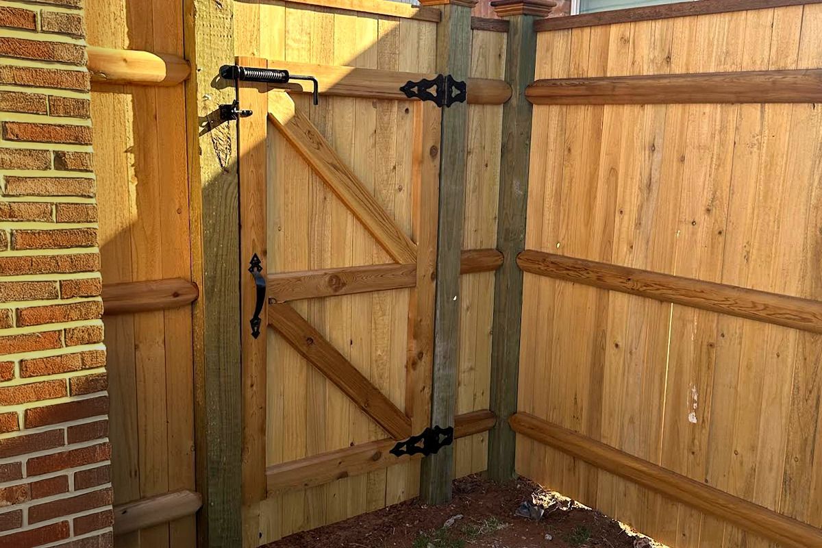 A wooden fence with a gate attached to it and a brick wall behind it.
