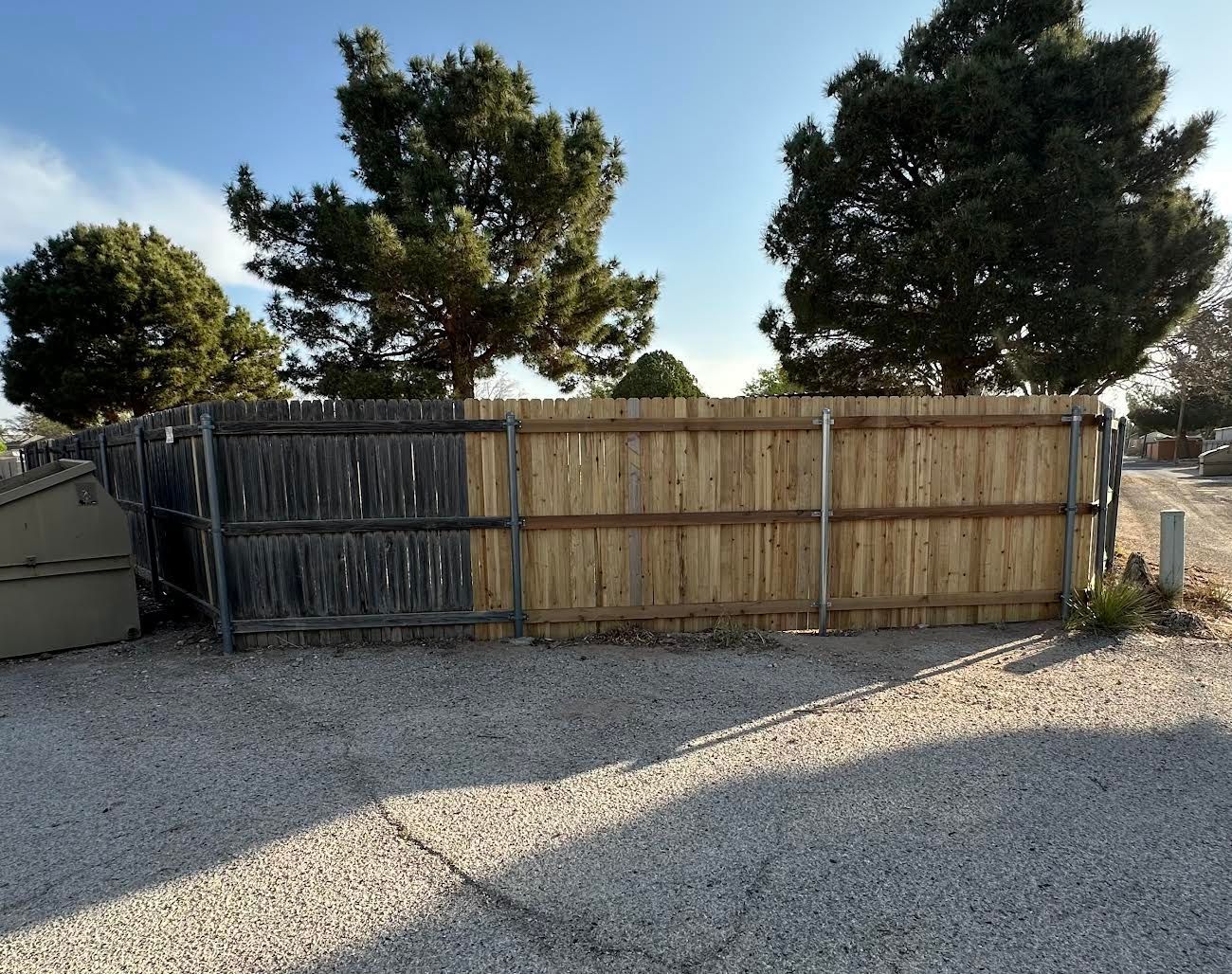 A wooden fence is surrounded by gravel and trees