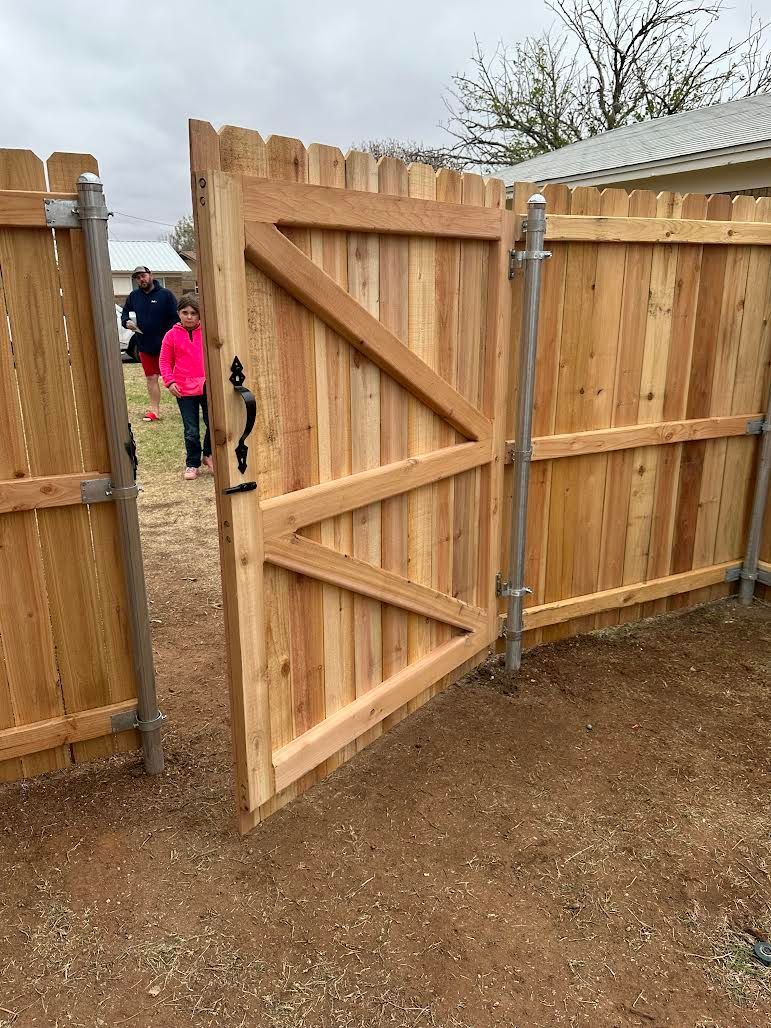 A wooden fence with a gate open and people standing behind it.
