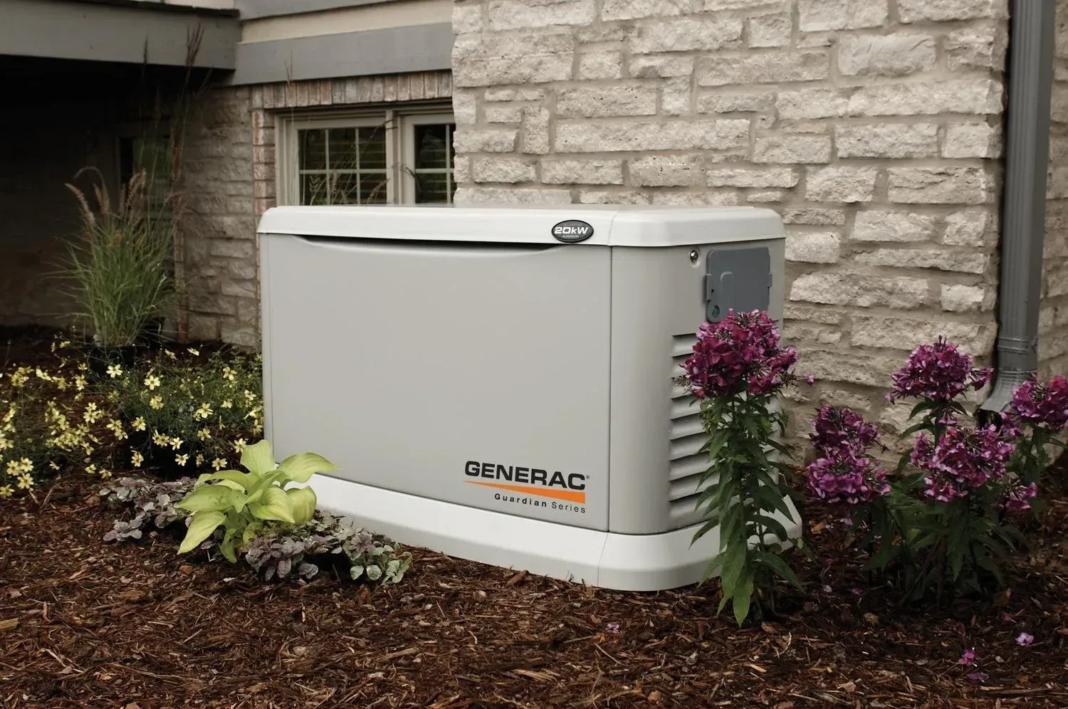 Outdoor Generac generator beside a stone house, surrounded by mulch and flowering plants