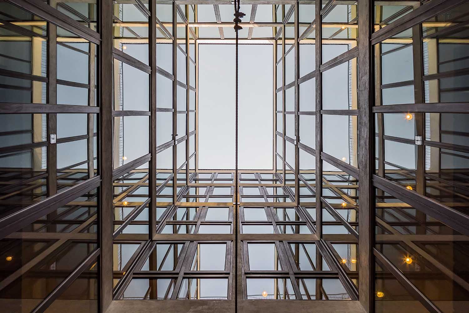 Mirando hacia arriba a una estructura arquitectónica de vidrio y acero. El cielo es visible a través de la abertura.