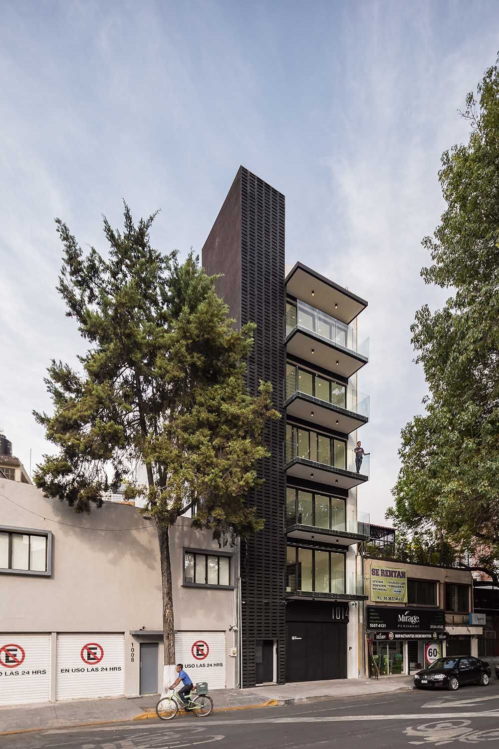 Edificio moderno de apartamentos con balcones y un árbol al costado. A nivel de calle, con acceso para coche y bicicleta.