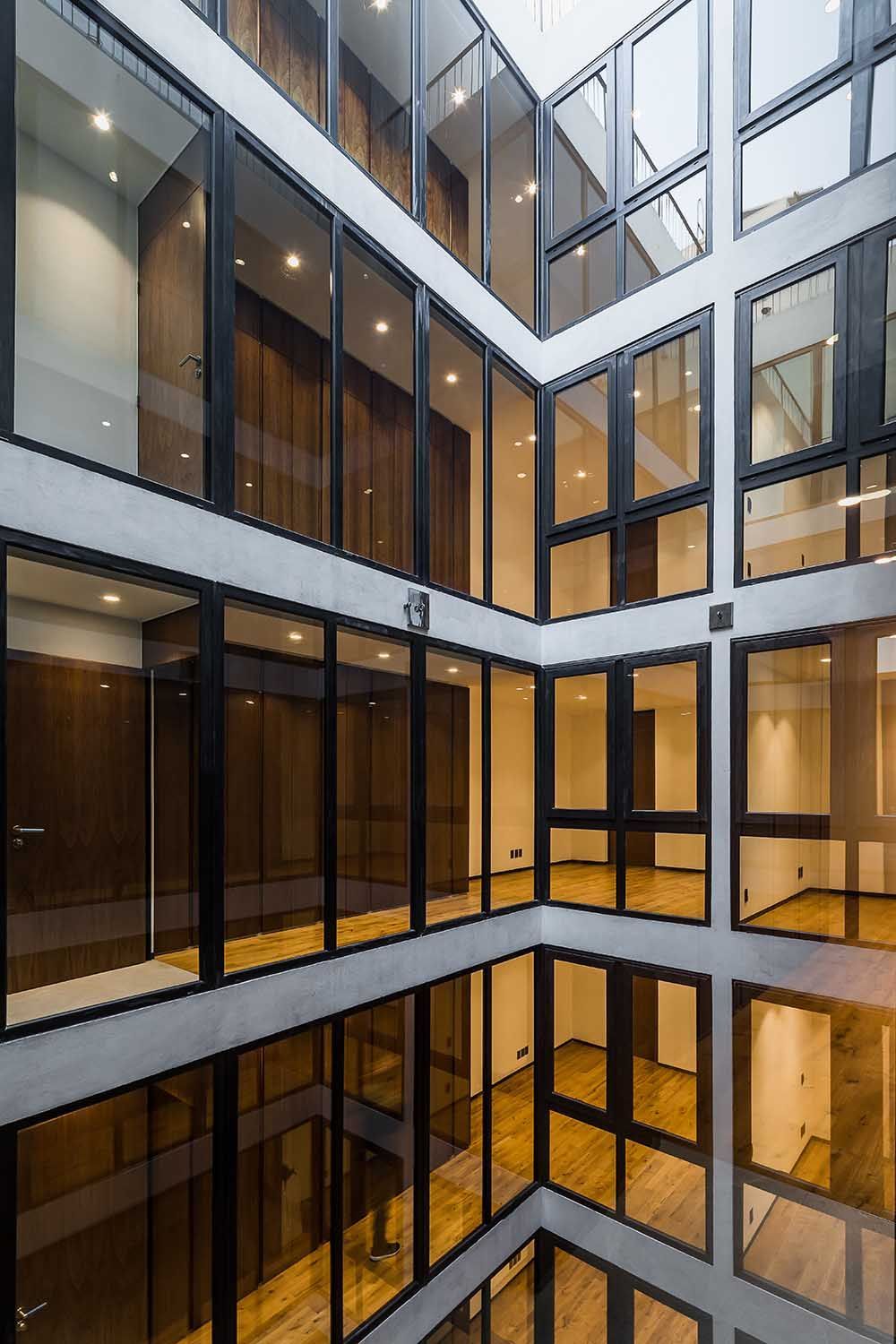 Interior de edificio de varios pisos con ventanas de vidrio y pisos de madera.