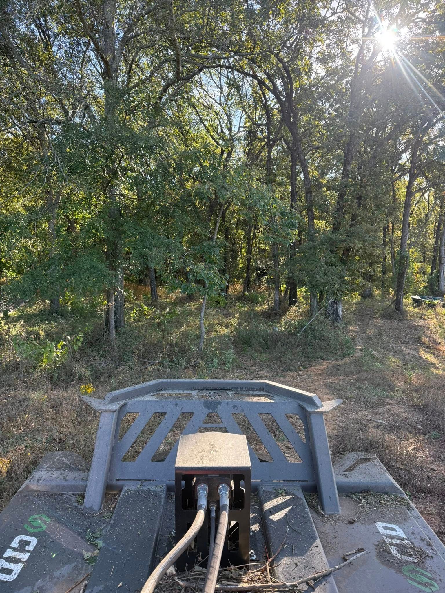 A metal attachment on the ground in a forest, with cables connected to a central base unit in front of a tree line.