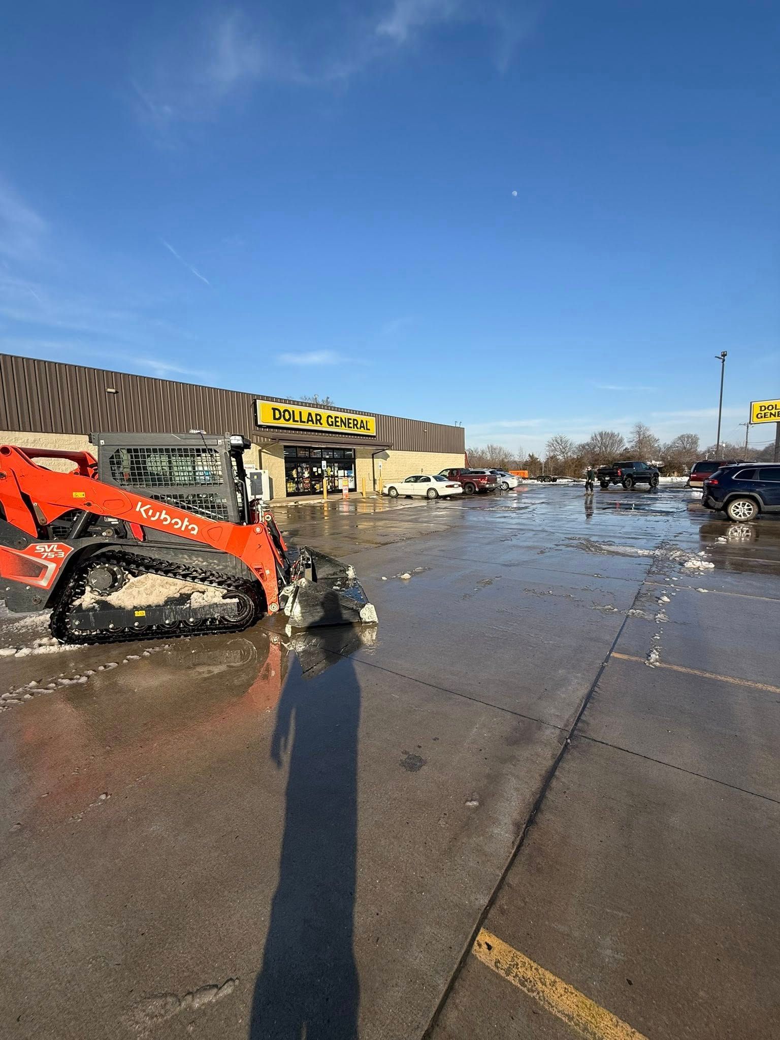 An orange skid-steer loader sits in a parking lot covered in scattered debris in front of a Dollar General store.