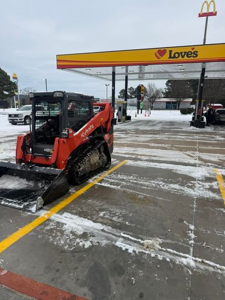 An orange Kubota track loader sits in a parking space at a snow-covered Love's gas station.