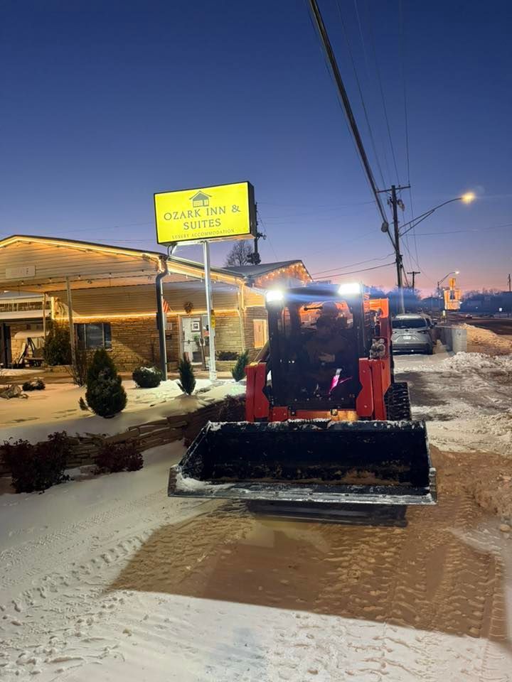 An orange skid steer loader clearing snow in front of an Ozark Inn and Coffee sign at dawn.