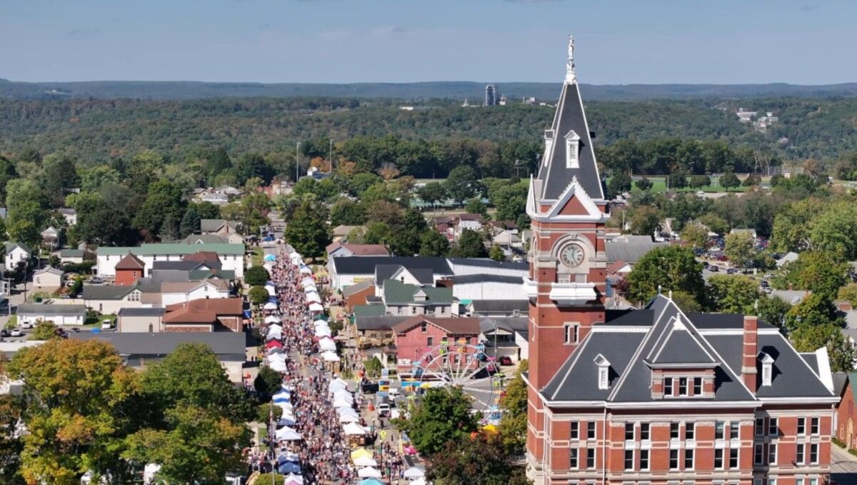 Brown and beige multi-story historic building with shutters, dormers, and a small front porch; iron fence.