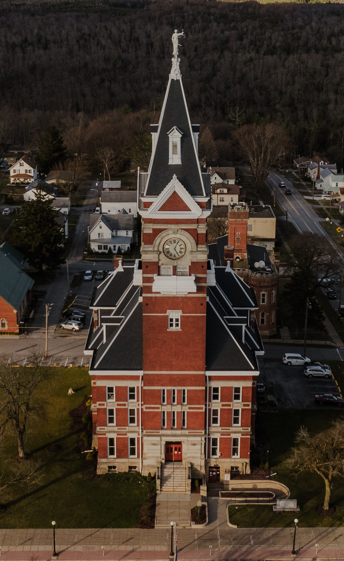 An aerial view of a historic red-brick courthouse with a prominent clock tower and a tall, dark roof spire.