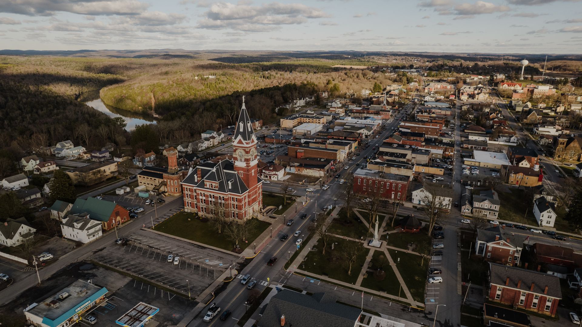 Aerial view of a small town square featuring a historic brick courthouse, a park with walkways, and surrounding buildings.