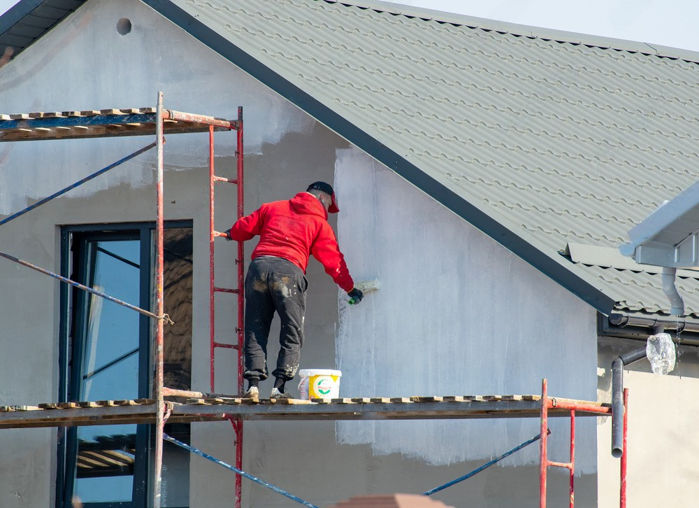 A man is painting the side of a house on a scaffolding.